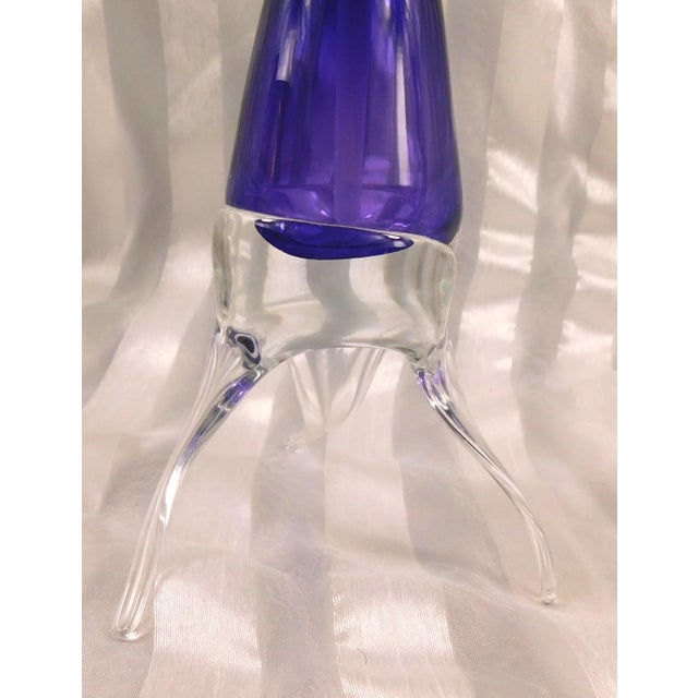 This is a very unusual art glass perfume bottle. The bottle itself is purple and that bottle sits in or on a clear base or...