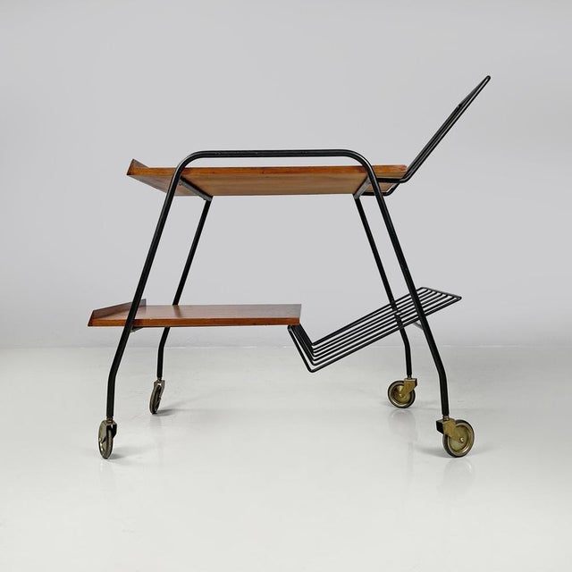 Italian mid-century modern wood and black metal trolley with brass wheels, 1960s Trolley with two wooden shelves. The...
