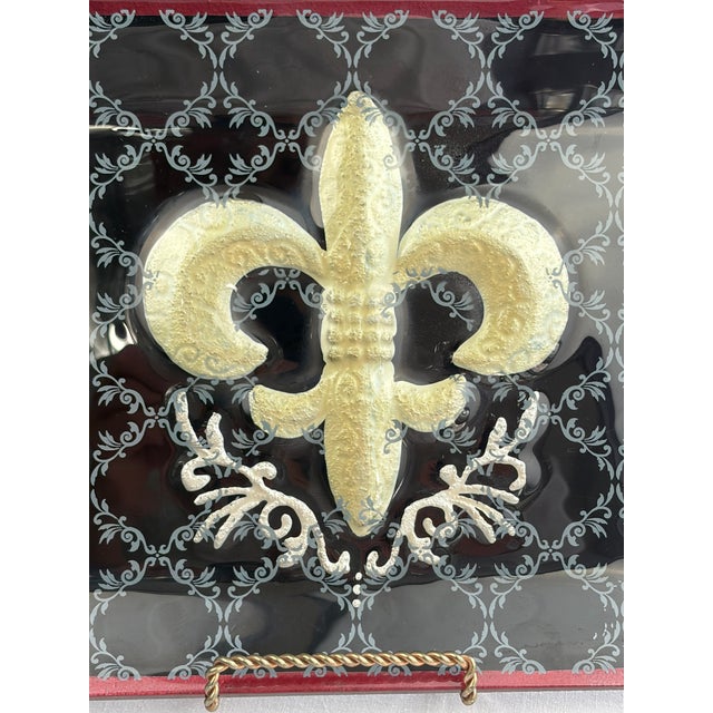 Hand-painted rectangular glass platter featuring a bold fleur-de-lis motif in gold and bronze tones, centered against a...