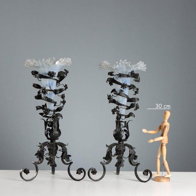 Pair of vases with a wrought iron base featuring a plant theme with leaves and flowers, a trumpet-shaped flower holder in...