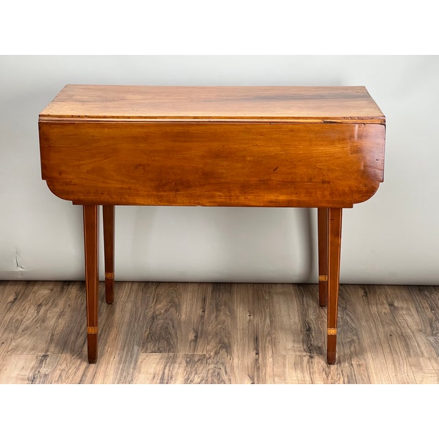 This Antique Hepplewhite Inlaid Maple Drop Leaf Table, dating to the early 19th century, is a refined example of...