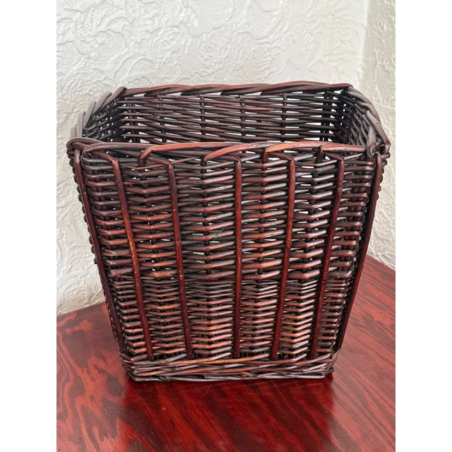Square woven rattan wicker waste basket with gently tapered sides. It has a rich dark ebony stain. Vertical stakes carry...