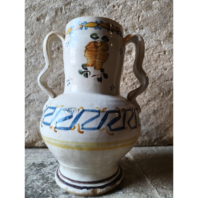 White glazed ceramic jug with a double, contoured handle, hand-decorated with a central polychrome plant motif and a blue,...