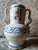 White glazed ceramic jug with a double, contoured handle, hand-decorated with a central polychrome plant motif and a blue,...