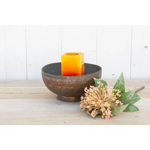 An antique engraved patinated water bowl with an intricate flower design on top and tribal motif across the center. This...