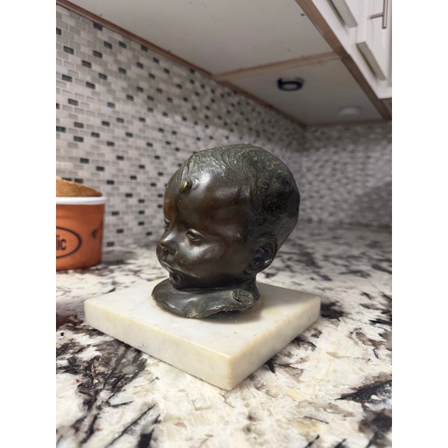 A substantial signed bronze infant bust mounted on a marble plinth. The sculpture features finely modeled facial details...