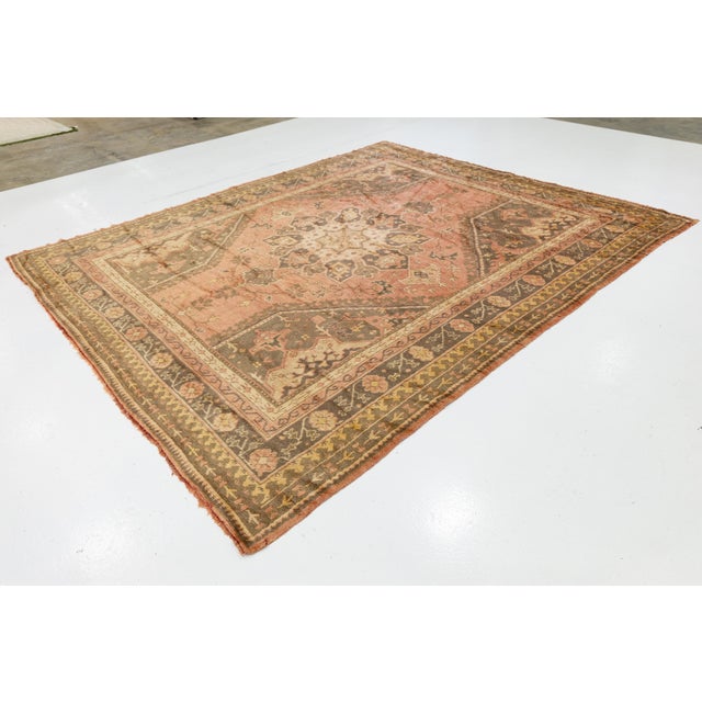 Antique Oushak wool rug featuring a luminous patina and soft, earthy tones. Handwoven with large-scale floral motifs and a...