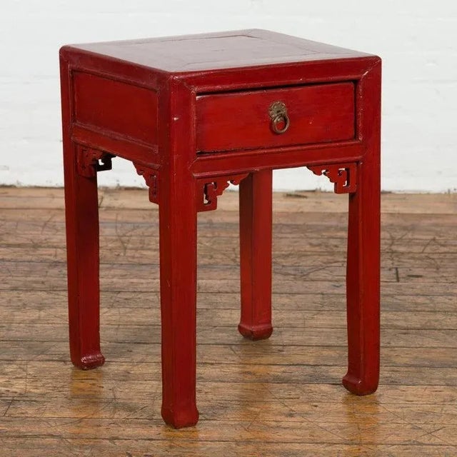 A vintage Chinese side table from the Mid-20th Century, with red lacquer, single drawer, carved spandrels and horse hoof...