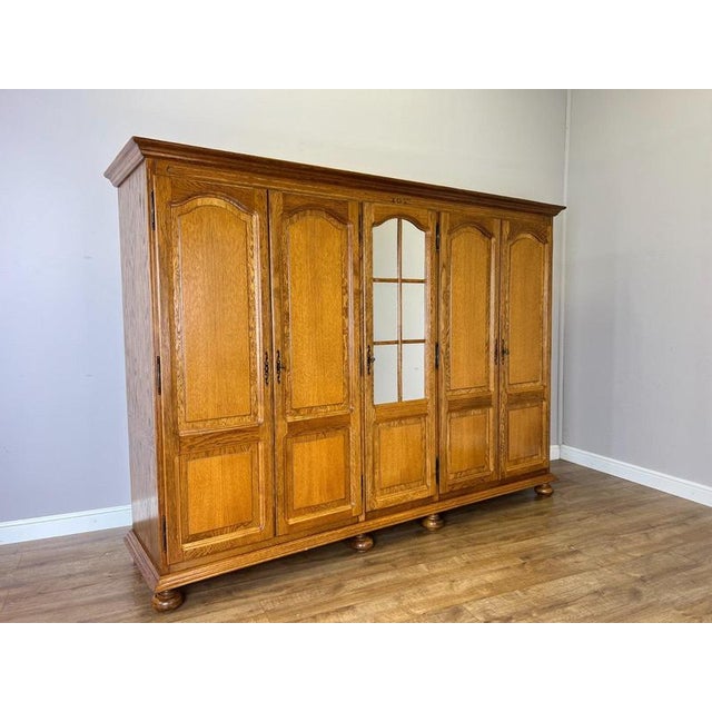 A substantial Vintage French wardrobe featuring five doors, a central mirrored panel and a warm Oak finish. The interior...