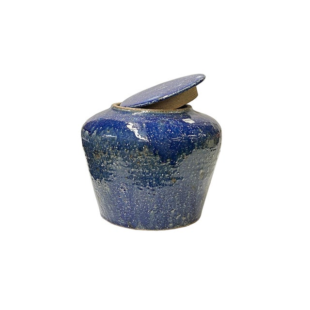 This charming ceramic jar captivates with its rustic, handcrafted appeal and striking deep blue glaze. The small, rounded...