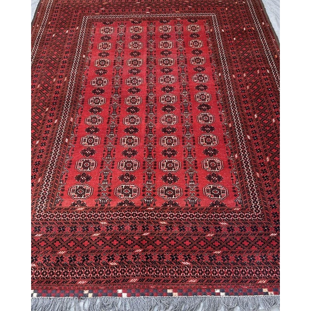 Three columns of ivory Tekke guls march down the deep crimson field of this hand-knotted Afghan Turkmen rug — twenty-four...