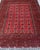 Three columns of ivory Tekke guls march down the deep crimson field of this hand-knotted Afghan Turkmen rug — twenty-four...