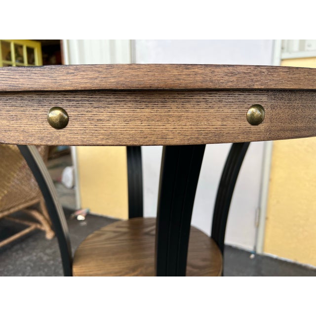 This round bar table features a rustic umber brown ash veneer top with nailhead trim and curved black metal legs. Measures...