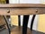 This round bar table features a rustic umber brown ash veneer top with nailhead trim and curved black metal legs. Measures...