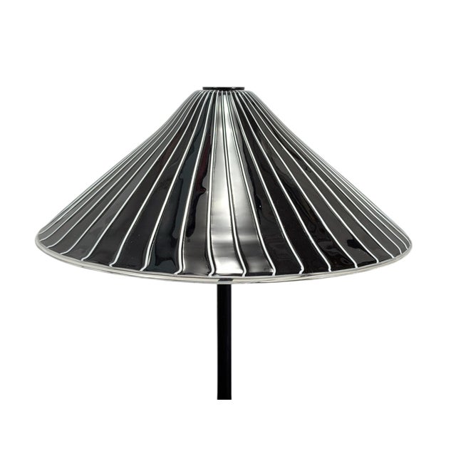 This modern table lamp stands out for its conical lampshade, crafted from glossy black glass embellished with thin white...
