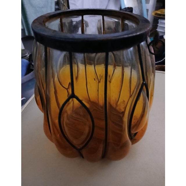 Gorgeous caged glass, hand blown, in an iron base with handle. Meant to hold a candle. Beautiful amber glass shading to...