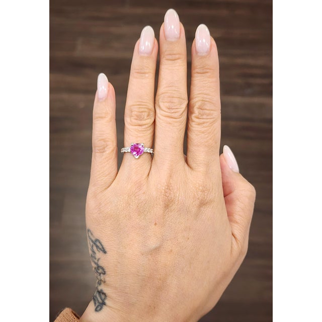 This striking cocktail ring showcases an approximately captivating 0.6 carat heart-cut pink sapphire, set in a sleek 18k...