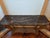 A commanding Neoclassical-style carved wood console table featuring an authentic inset black marble top with striking...