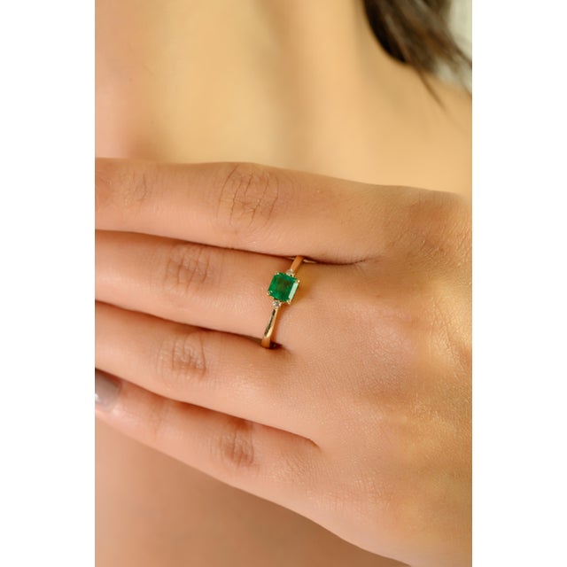 This elegant three-stone ring features a square-cut natural emerald at the center, weighing approximately 0.38 carats, set...