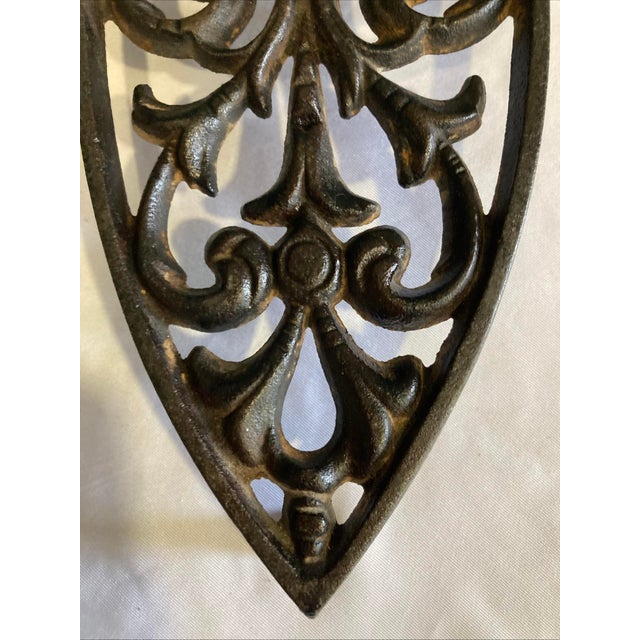 This vintage Griswold cast iron trivet features an elegant scrollwork design framed in a shield-shaped form. Griswold is...