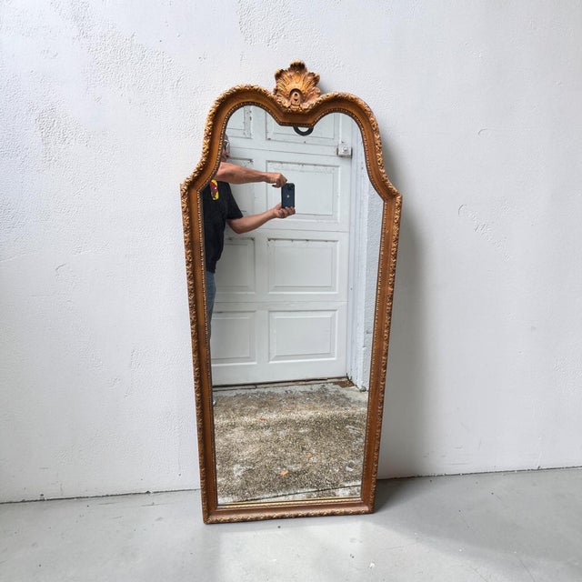 A striking vintage Hollywood Regency wall mirror featuring an elegant Rococo Revival silhouette with a sculptural arched...