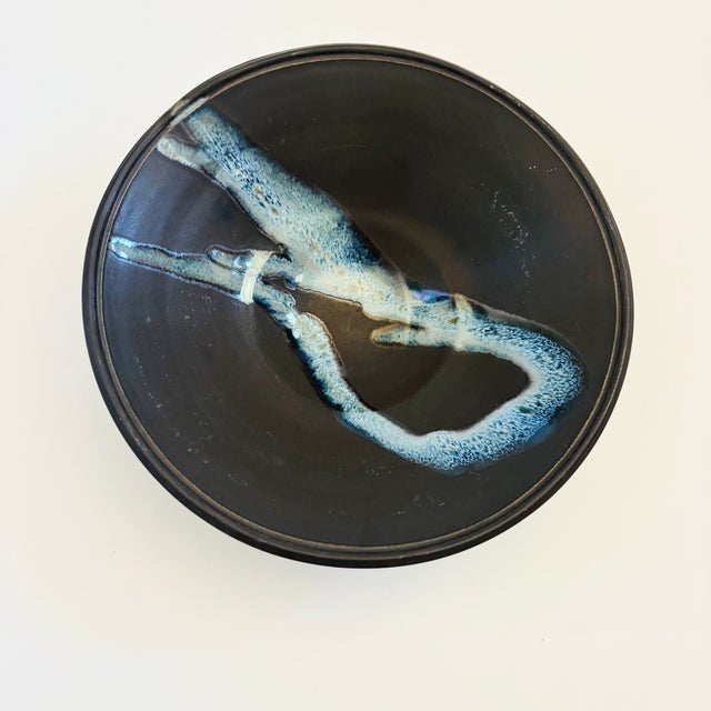 A large circular vintage studio pottery bowl. Matte black glaze with a glossy blue abstract design in the center. Ribbed...