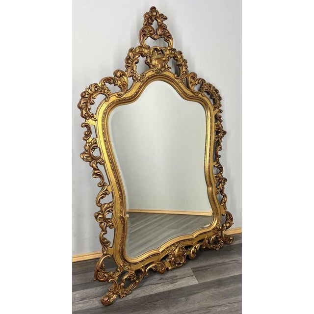 A richly detailed Vintage French mirror featuring an ornate gold frame with intricate scrolling and carved decorative...