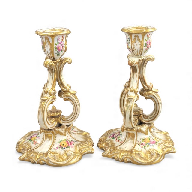 A refined pair of Regency-period Derby candlesticks with broad rococo scroll bases, soft shell curves and warm original...