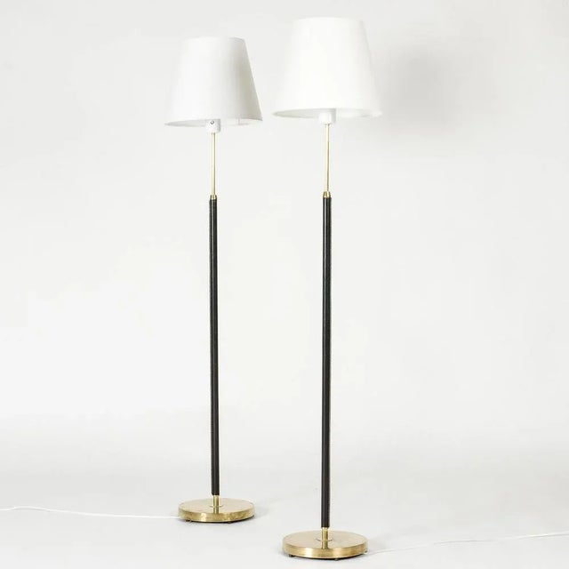 Pair of elegant floor lamps from Falkenbergs Belysning, made from brass. Sleek stems dressed with black leather,...