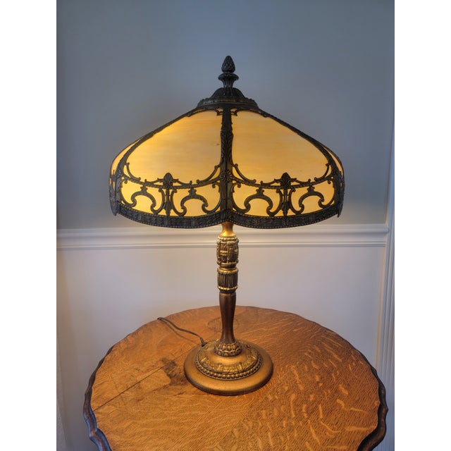 Antique Rainau cast metal table lamp featuring an ornate Tudor Revival design with an eight-panel caramel slag glass...