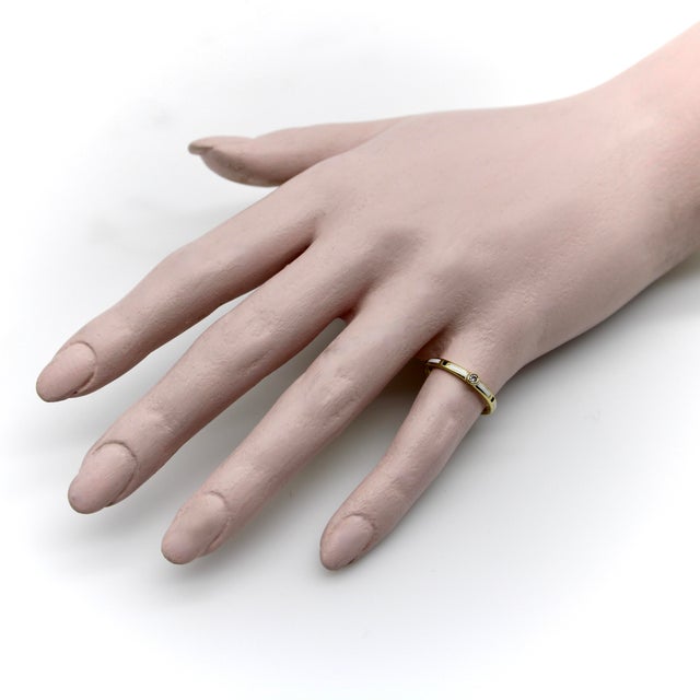 This 18k gold band is detailed with a rhythmic patten of white and black enamel, accented by a bezel set diamond....