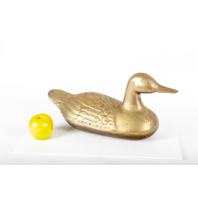 A solid and weighted cast brass duck form sculptural door stop modeled in a traditional resting pose, with a softly...