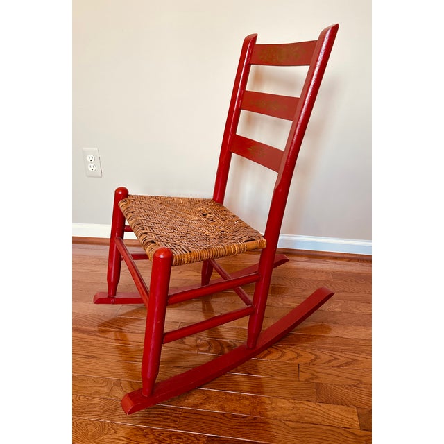 Early 20th Century ladder-back rocking chair featuring a woven seat and decorative gold stenciling on the slats.
