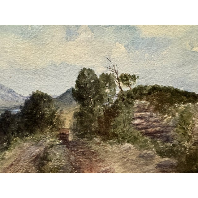 Original watercolor on paper depicting a mountainous landscape with a winding dirt road, trees, rocky outcrops and a broad...