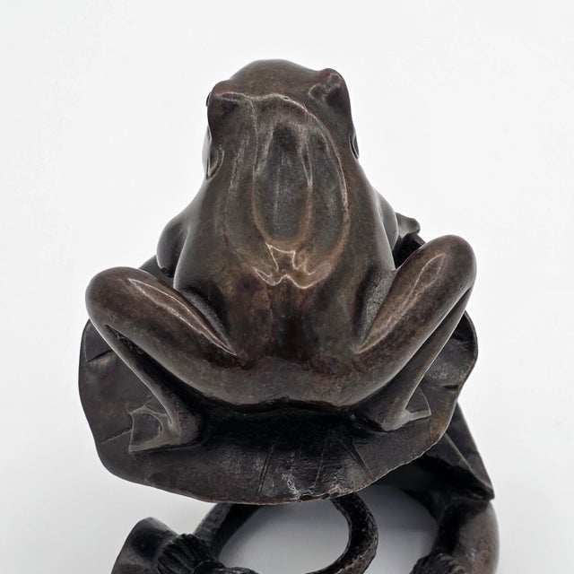 A finely detailed Japanese bronze okimono sculpture depicting a frog perched on a lotus leaf, with a coiled stem-form base...