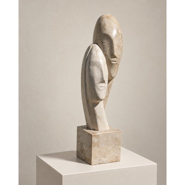 An evocative late-20th-century sculpture depicting two elongated, interlocking faces in a quiet embrace. The abstracted...