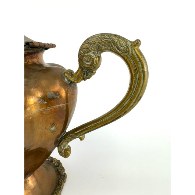 A substantial vintage copper teapot accented with ornate brass detailing, crafted in a classic French-inspired form. The...