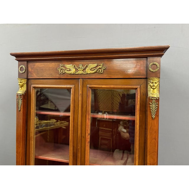 Small Empire-style walnut and cherrywood bookcase, inspired by the Egyptian Revival, opening with two doors. The interior...