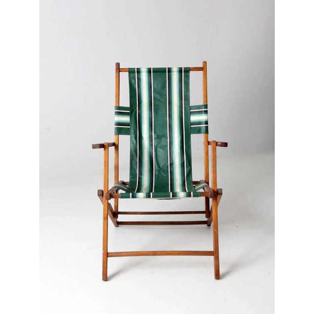 A charming mid-20th century deck chair featuring a classic wooden frame paired with bold green striped canvas upholstery....