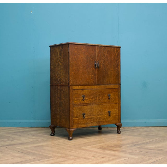 A tiger oak linen press dating from the 1930s, offering practical storage in a compact piece. Raised on Queen Anne...