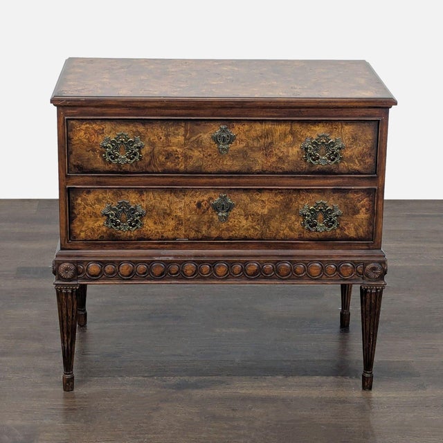 This vintage nightstand by FF Fine Furniture features two spacious drawers with detailed, ornate brass handles. The wood...