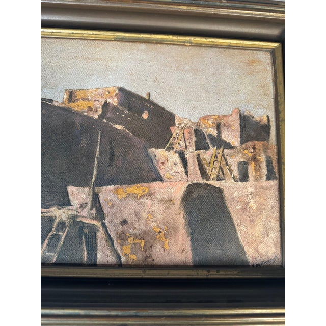 An original oil, likely on canvas board: a multi-storey stepped adobe pueblo with wooden ladders and a kiva ladder in the...