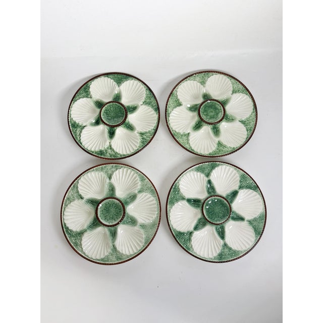 Elegant set of four French oyster plates in glazed ceramic, featuring six shell-shaped wells surrounding a central sauce...