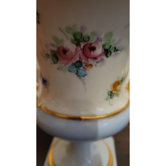 Vintage small ceramic urn with square base, the iron base has four legs with fleur de lis designs. The handles depict two...