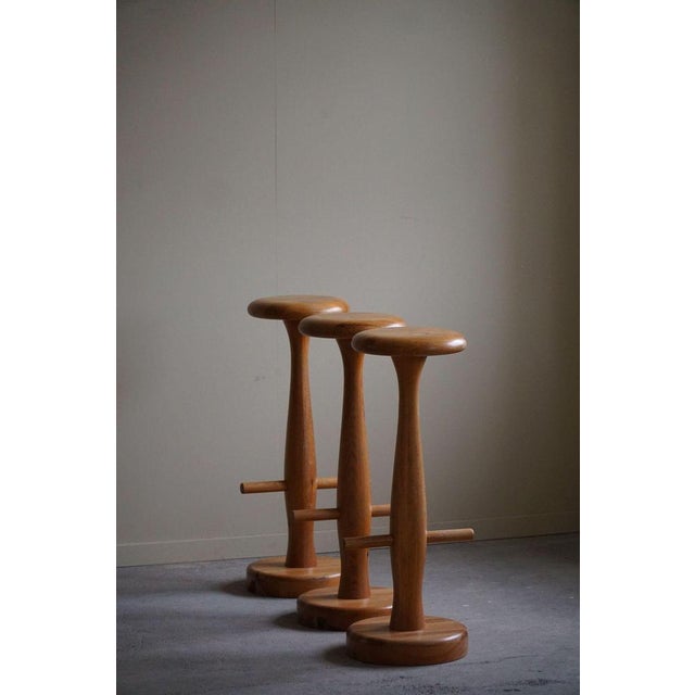 A charming set of three round bar stools crafted from solid oak, showcasing a sleek, hourglass-shaped silhouette. These...