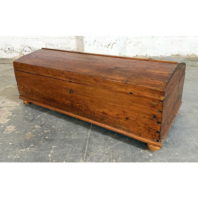 This antique pine chest features a gently domed lid, dovetailed construction, and a warm, timeworn surface with abundant...