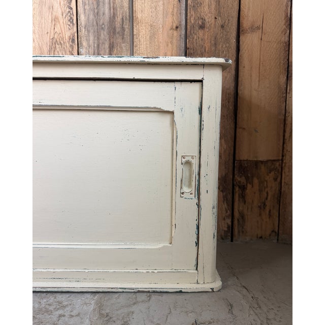 This vintage low cabinet is distinguished by its elongated shape, molded panels, and original off-white patina. Its...