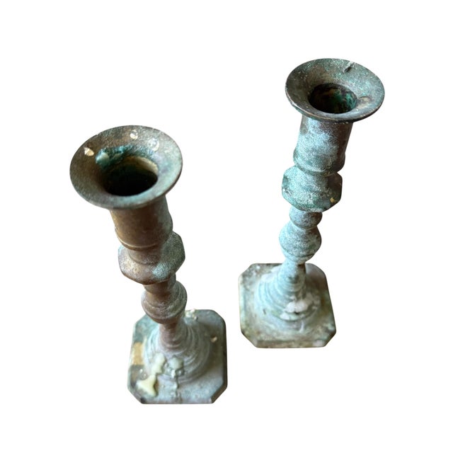 A sculptural pair of vintage brass candlesticks featuring elegantly turned silhouettes and a beautifully aged verdigris...