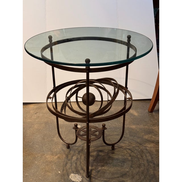 Wrought iron table with a circular glass top resting on a ring supported by three uprights terminating in ball finials....