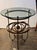 Wrought iron table with a circular glass top resting on a ring supported by three uprights terminating in ball finials....
